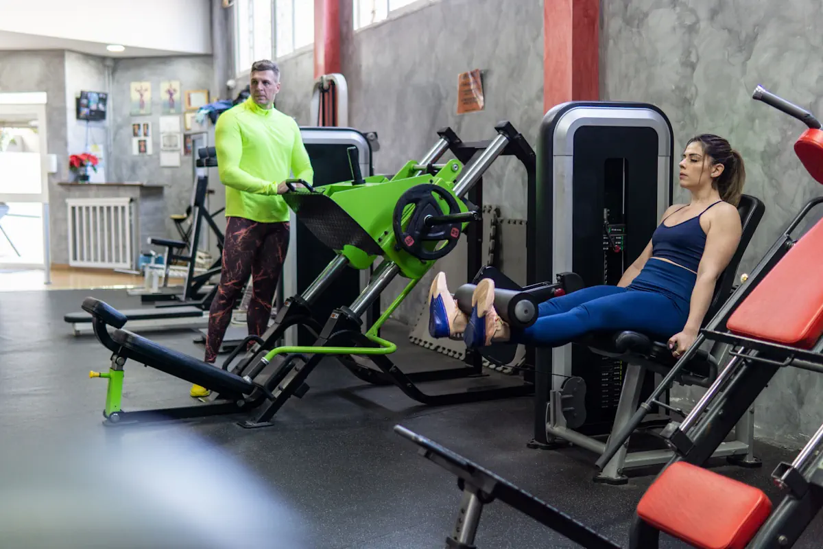 Solutions de financement d’équipements de gym sur mesure par Lease2Grow 1 Entraîneur personnel coachant une jeune femme, exercices pour les jambes avec machine au gymnase.