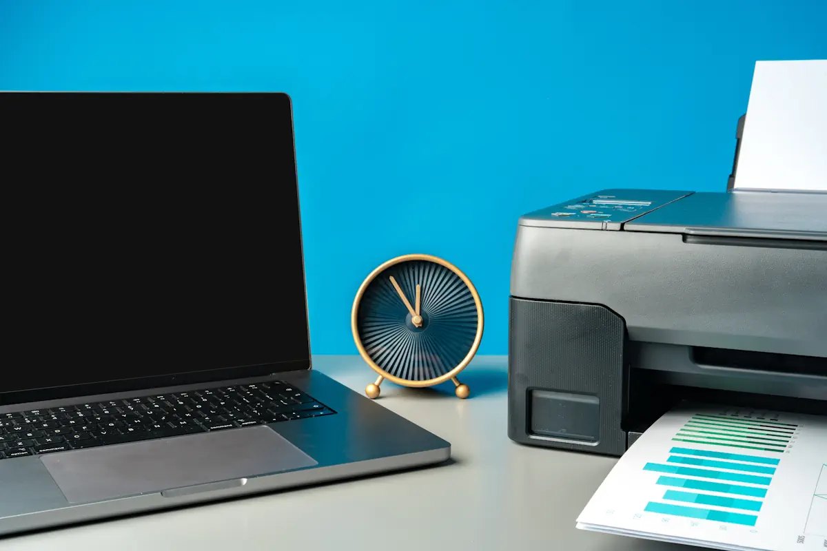 Modern printer with paper and laptop on table in office