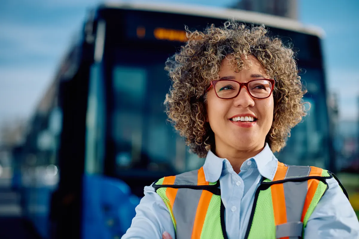 A woman transportation worker smiling in front of a parked bus